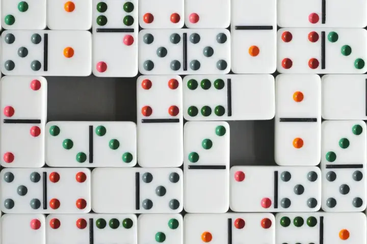 Wiele białych kostek do gry w domino z kolorowymi kropkami (zielonymi, czerwonymi, szarymi i pomarańczowymi) ułożonych w rzędy.