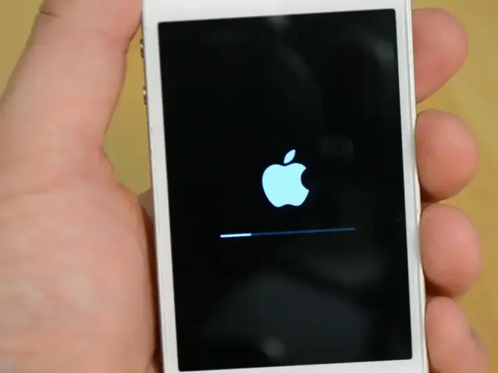 Dłoń trzyma iPhone'a z logo Apple i paskiem postępu, wskazującym na proces hard reset iPhone.