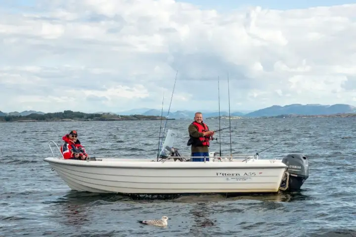 Zwei Männer genießen das Angeln in Norwegen auf einem Boot. Eine Möwe schwimmt im Wasser.