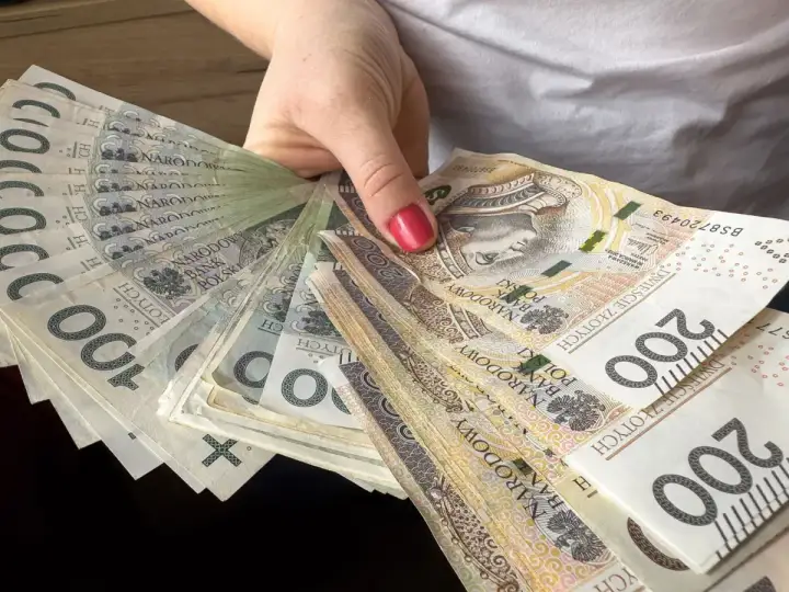 Dłoń trzyma wachlarz polskich banknotów 100 i 200 zł. To może być nagroda jubileuszowa nauczycieli.