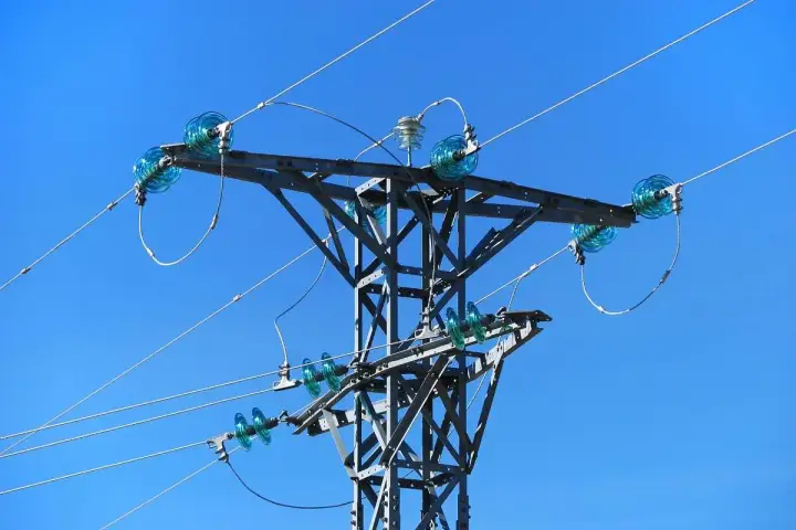 Metalowa konstrukcja słupa energetycznego z niebieskimi izolatorami, przez które biegnie linia średniego napięcia.