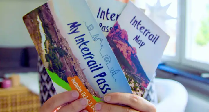 Ręce trzymają broszurę "My Interrail Pass" i mapę. To świetny sposób na podróżowanie po Europie, jeśli zastanawiasz się interrail co to.