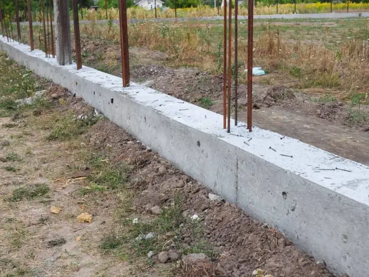 Solidna podmurówka ogrodzenia panelowego z wystającymi prętami zbrojeniowymi, gotowa na montaż.