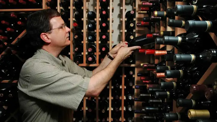 Uomo in cantina sceglie tra bottiglie di vino, tra cui uve cabernet.