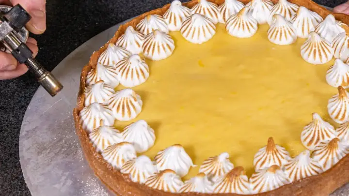 Ein köstlicher Lemon Curd Kuchen mit Baiserhauben wird mit einem Brenner karamellisiert.