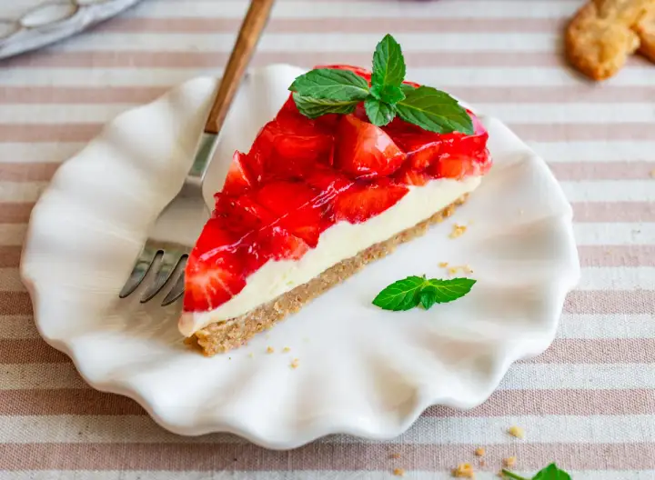 Ein Stück Erdbeer-no-bake-cheesecake mit frischer Minze auf einem weißen Teller, daneben eine Gabel.
