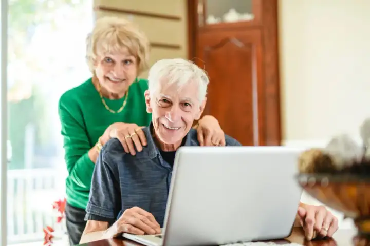 Couple souriant devant un ordinateur, discutant de l'obligation alimentaire en EHPAD et des impôts.