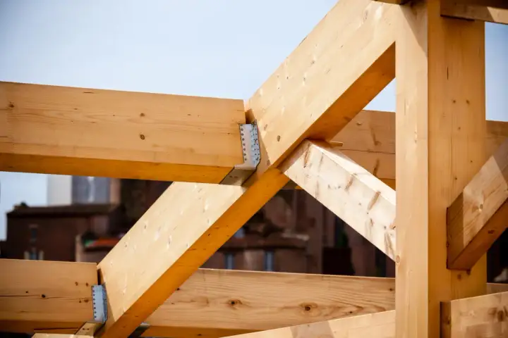 Estructura de vigas de madera clara, parte de techos de madera en construcción, con uniones metálicas visibles.