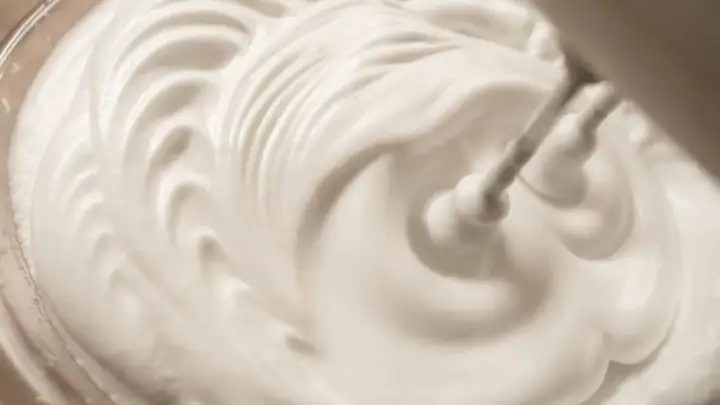 Sahne steif schlagen ohne Sahnesteif: Ein Handmixer formt cremige Wellen in der weißen Masse.