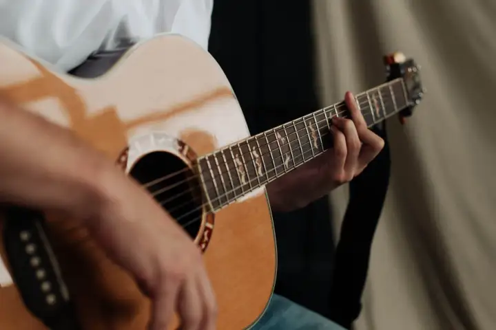 Dłoń grająca na gitarze akustycznej. Zastanawiasz się, ile trwa nauka gry na gitarze? To zależy od Ciebie!