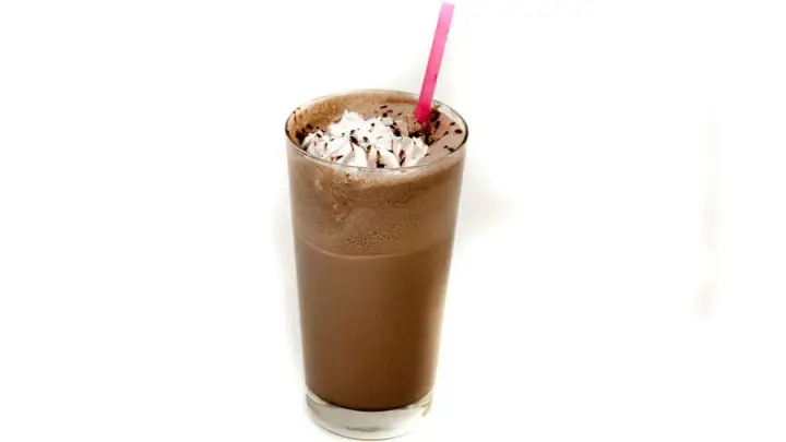 Un delizioso frappè al cioccolato, guarnito con panna montata e scaglie di cioccolato, pronto per essere gustato con una cannuccia rosa.