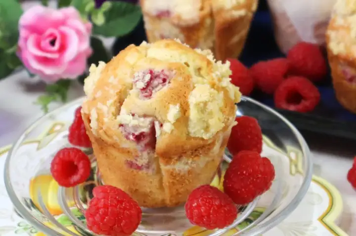 Pyszne muffinki z malinami, posypane kruszonką, otoczone świeżymi malinami.