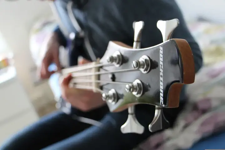 Osoba gra na gitarze basowej, wydobywając głębokie dźwięki na basie.