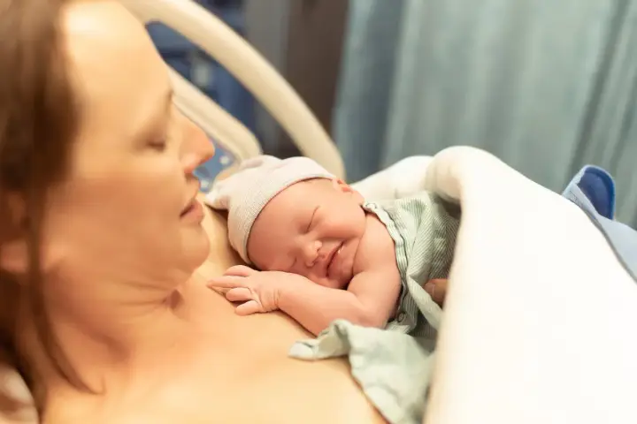 Noworodek śpi na piersi mamy, przygotowując się do karmienia. To piękny początek laktacji i więzi.