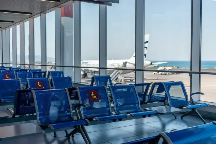 Puste, niebieskie siedzenia na lotnisku w Kalabrii, z widokiem na samolot Aegean i morze.