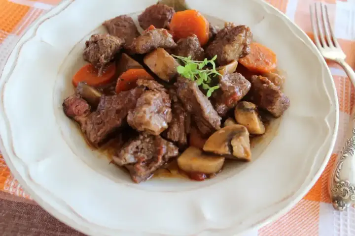 Bœuf bourguignon: duszona wołowina z marchewką i pieczarkami, podana na talerzu.
