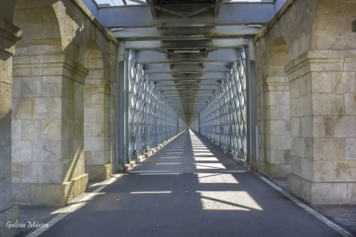 El **puente internacional Tui** se alza imponente, un túnel de metal y piedra que se pierde en la distancia, proyectando sombras geométricas sobre el asfalto.