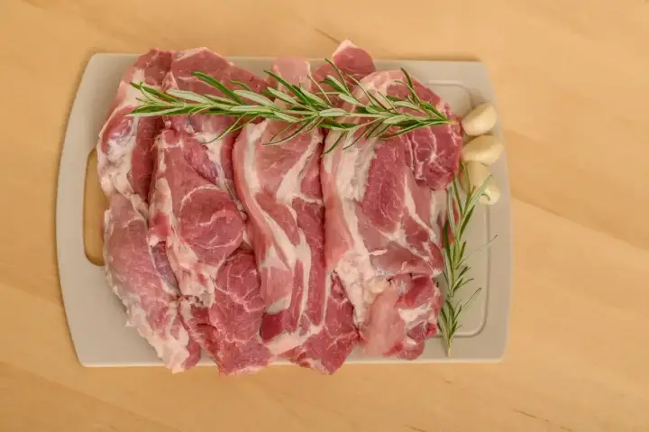 Surowe kawałki wieprzowiny z rozmarynem i czosnkiem, idealne jako jakie mięso do bigosu.