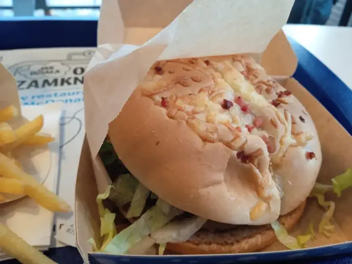 Pyszny burger drwala z chrupiącym bekonem i serem, w papierowym opakowaniu, obok porcji frytek.