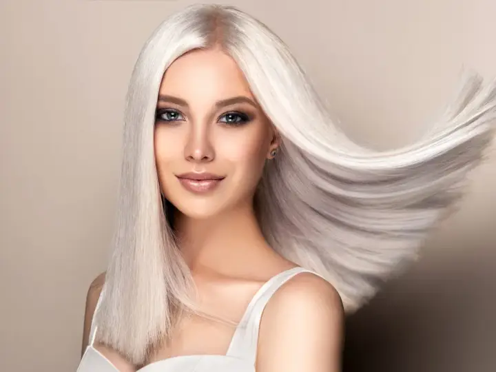 Kobieta z olśniewającymi, falującymi włosami w odcieniu perłowy blond. Jej spojrzenie przyciąga uwagę, a makijaż podkreśla urodę.