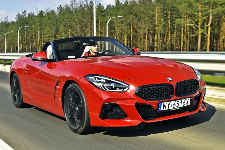 Czerwone z4 bmw z opuszczonym dachem pędzi po drodze, kierowca w czapce z daszkiem cieszy się jazdą.