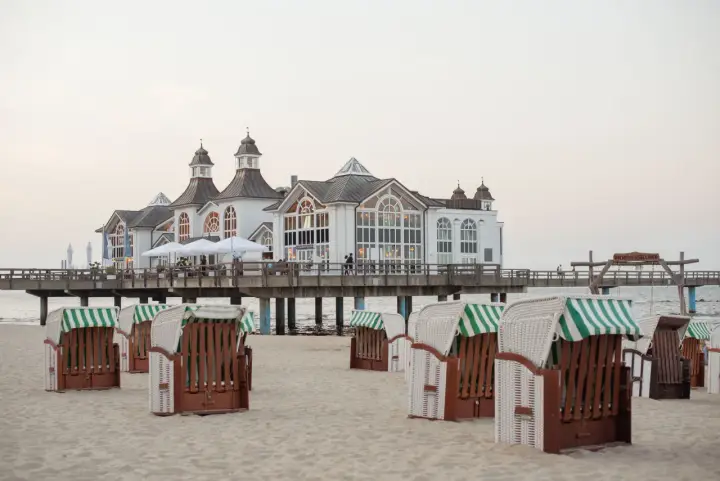 Plaża na wyspie Rugia z charakterystycznymi koszami plażowymi i molo prowadzącym do białego pawilonu.