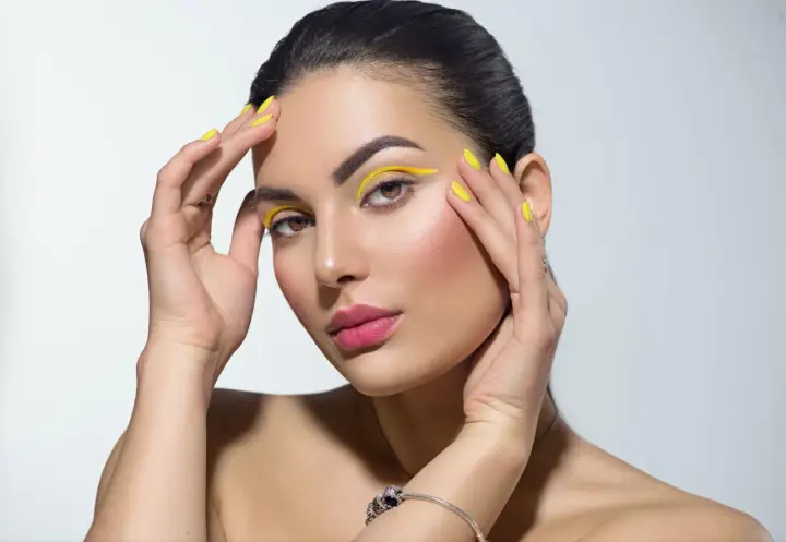 Mujer con un atrevido doble eyeliner amarillo y uñas a juego.