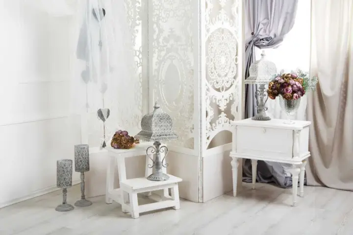 Delikatny salon w stylu shabby chic. Białe meble, ażurowa parawan, świeże kwiaty i ozdobne latarenki tworzą romantyczny nastrój.