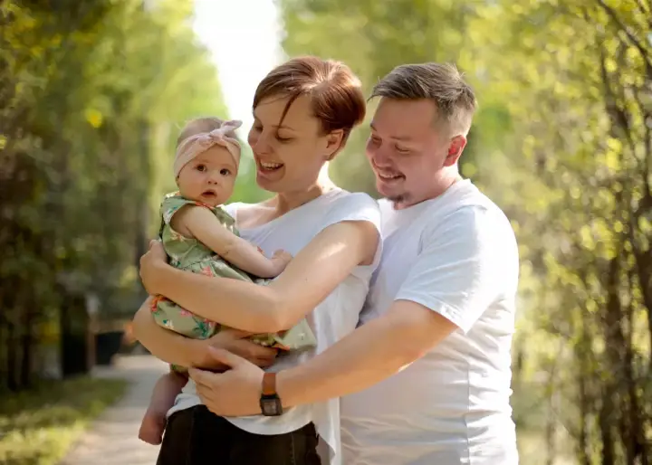 Szczęśliwa rodzina z córeczką w letnim parku. Mama tuli dziecko, tata obejmuje ich. Idealne babciowe warunki na spacer.