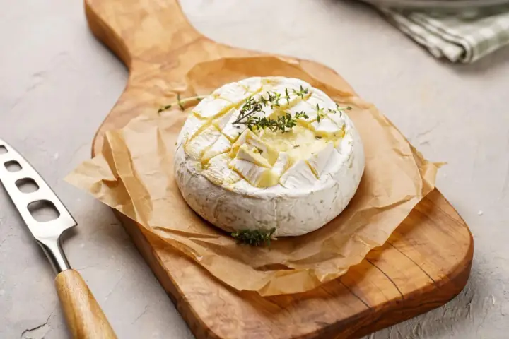 Pyszny camembert z grilla, zapieczony z ziołami, na drewnianej desce. Idealny do maczania.