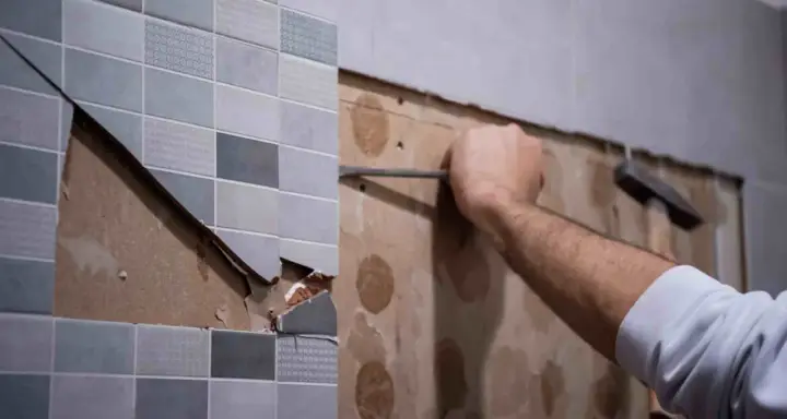 Persona usando una espátula para quitar azulejos de una pared.