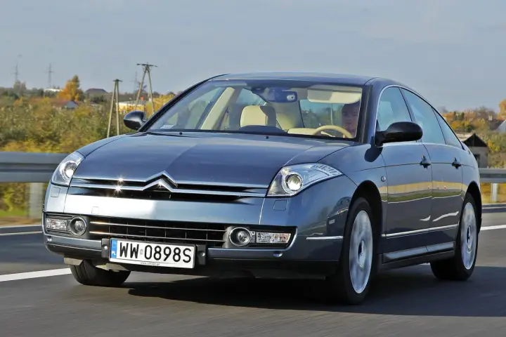 Elegancki Citroën C6 w kolorze granatowym jedzie po drodze. Wnętrze z jasną tapicerką i kierowcą.