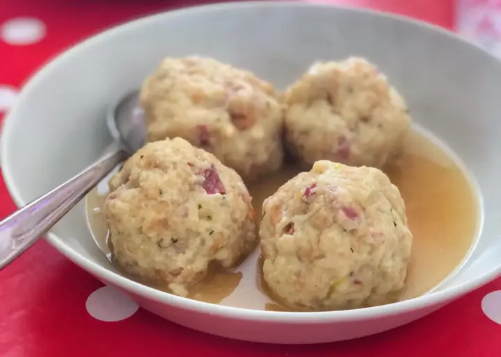 Canederli in brodo, uno dei piatti tipici del Trentino Alto Adige, serviti in una ciotola bianca su un tovagliolo rosso a pois bianchi.