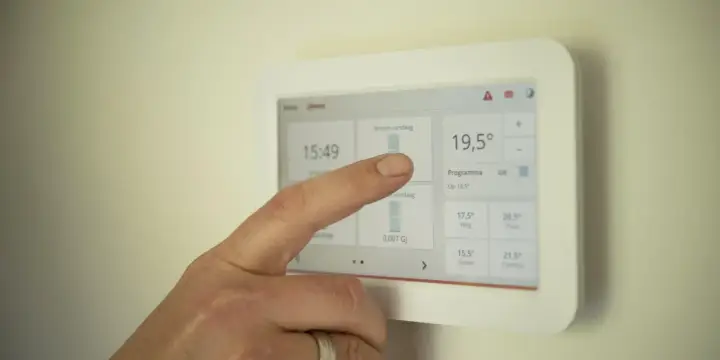 Un doigt interagit avec un écran tactile de domotique affichant la température et les programmes.