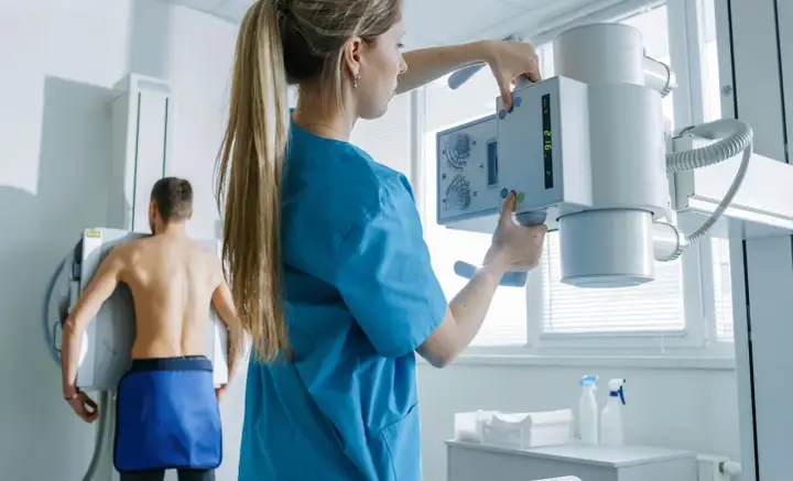 Technik przygotowuje aparat RTG do badania pacjenta. To właśnie RTG co to jest – badanie obrazowe wykorzystujące promieniowanie rentgenowskie.