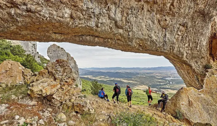Senderismo Navarra: grupo de excursionistas admira un paisaje montañoso desde debajo de un arco de roca natural.