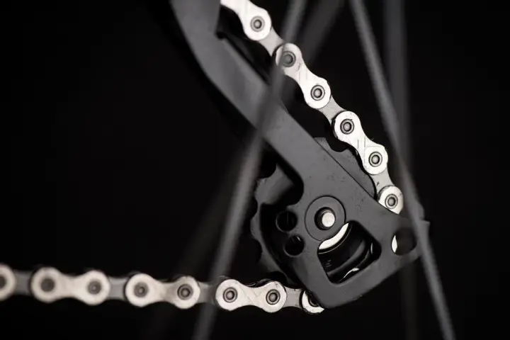 Zbliżenie na mechanizm przerzutki z łańcuchem rowerowym. Widać ogniwa i rolki, kluczowe dla łańcuch rowerowy wymiary.