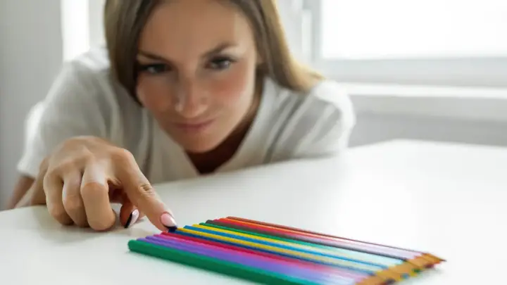 Kobieta z uwagą układa kolorowe kredki, co może symbolizować potrzebę porządku w chorobie OCD.