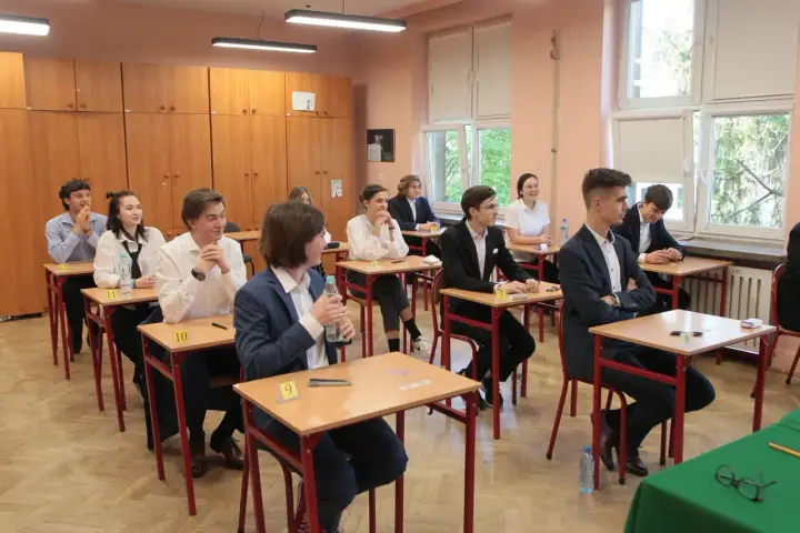 Uczniowie siedzą w ławkach podczas egzaminu. Zastanawiają się, ile trwa matura z biologii, skupieni na zadaniach.