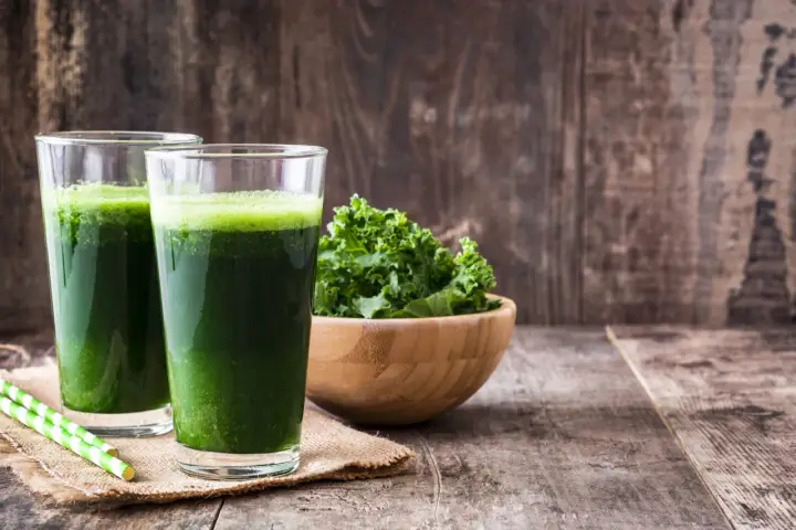 Dwa szklanki zielonego smoothie, miska jarmużu i słomki. Idealne na śniadanie zgodne z dietą sirtuinową.