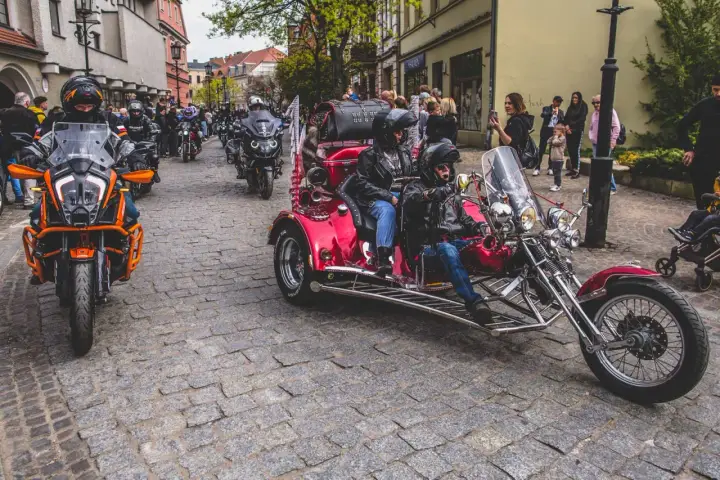 Parada motocykli i trójkołowców na brukowanej ulicy. W tle widzimy ludzi i budynki. To może być początek podróży szwecja motocyklem.