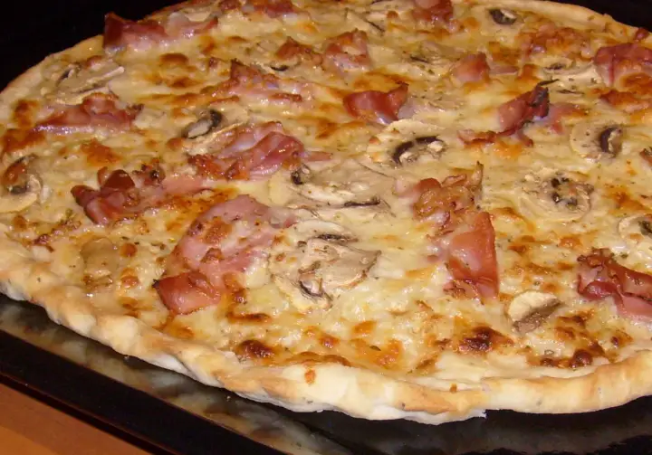 Pyszna pizza carbonara z chrupiącym boczkiem, pieczarkami i ciągnącym się serem. Idealna na szybki obiad.