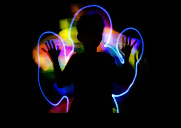 Silueta de niño jugando con light painting, creando auras de colores vibrantes a su alrededor.