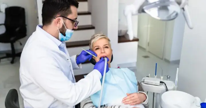 Dentysta wykonuje piaskowanie zębów u pacjentki, która siedzi na fotelu dentystycznym.