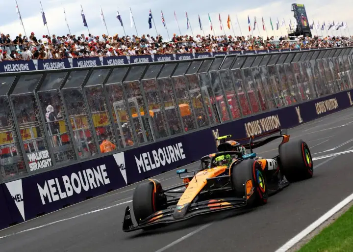 Un coche de Fórmula 1 naranja y negro acelera en Melbourne. Los aficionados vitorean. ¡Qué ganas de que empiece la Fórmula 1 2026!