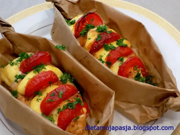 Dwa porcje kurczaka w papirusie z pomidorami i serem, posypane natką pietruszki.