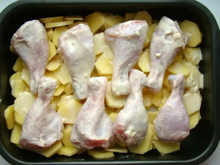 Osiem pałek kurczaka w sosie, ułożonych na plastrach ziemniaków w brytfannie. Idealne do pieczenia, by uzyskać chrupiące pałki z kurczaka w piekarniku.