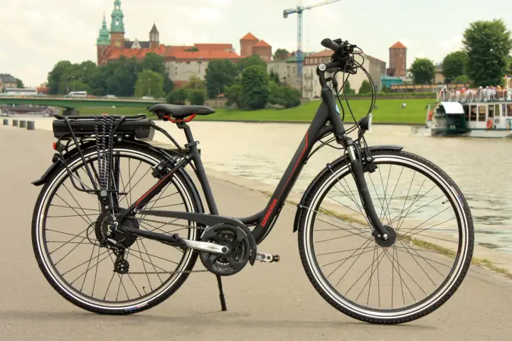 Czarny rower elektryczny z baterią na bagażniku, gotowy do jazdy po bulwarach z widokiem na Wawel.