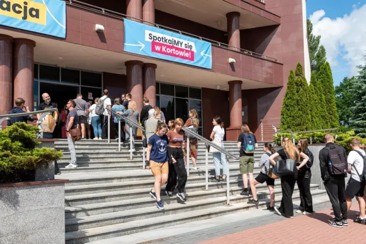 Grupa młodych ludzi schodzi po schodach przed budynkiem, gdzie wisi baner "Spotkajmy się w Kortowie!". To idealne miejsce na rozpoczęcie studiów w Olsztynie.