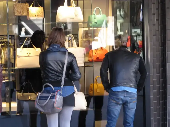 Coppia osserva vetrina di borse Benetton a Riccione. Lei con giacca in pelle, lui con giubbotto.